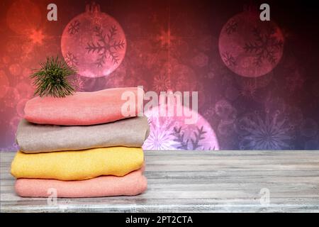 Vorlage für weihnachtsverkauf. Stapel von bunten gestrickten gemütlichen warmen Kaschmirpulvern auf einem Holztisch isoliert vor abstraktem Weihnachtshintergrund. Stockfoto