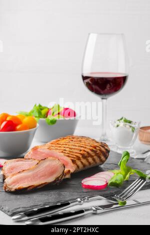 Gegrilltes Rindfleisch Steak medium auf der Steintafel mit frischem Gemüse und einem Glas Rotwein. Foto mit geringer Tiefenschärfe. Stockfoto