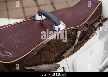 Brauner Motorrad-Sattelbezug aus Kunstleder (PVC oder PU), gerissen, um den Schwamm im Inneren zu sehen. Stockfoto