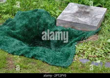 Kleines offenes Grab bedeckt mit einer grünen Matte vor Urnenbestattung auf einem Friedhof Stockfoto