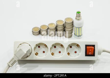 Stapel aufsteigender Euro-Münzen mit einer Glühlampe und Steckdosenleiste. Energiesparkonzept. Stockfoto