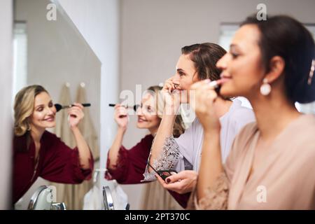 Die Damen wollen so hübsch wie möglich aussehen. Eine Gruppe wunderschöner junger Brautjungfern, die sich am Morgen der Hochzeit vor einem Spiegel schminken Stockfoto