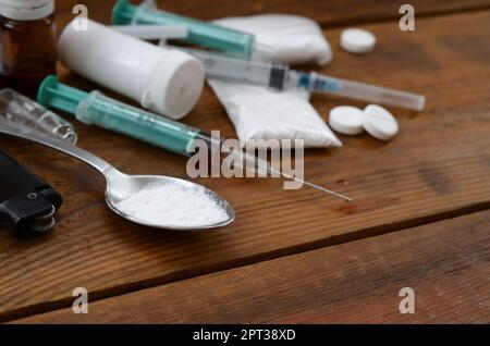 Eine Menge von Betäubungsmitteln und Geräte für die Zubereitung von Drogen liegen auf einem alten Holztisch. Drogendealer Material. Heroin und Methamphetamin im raw Stockfoto