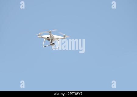 Big White drone schwebt in einem hellen wolkenlosen blauen Himmel, Radio Control Helicopter mit tragbaren Videokamera Versorgung Stockfoto