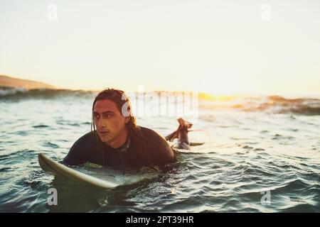 Mit der Flut aufstehen und mit dem Strom gehen. Ein junger Mann, der auf einem Surfbrett im Meer paddelt Stockfoto