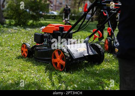 Gärtner für kommunale Dienstleistungen Mann, der Rasenmäher zum Rasenmähen im Stadtpark verwendet. Stockfoto