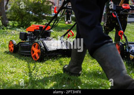 Gärtner für kommunale Dienstleistungen Mann, der Rasenmäher zum Rasenmähen im Stadtpark verwendet. Stockfoto