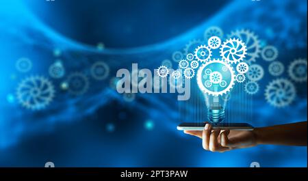 Mann Hand hält Smartphone und kreative Glühbirne mit Zahnrad innen und Technologie Hintergrund. Innovation Business Idea Knowledge, Planing Strategy, A Stockfoto