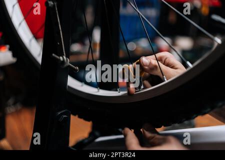 Nahaufnahme eines unbekannten Mechanikers, der die Fahrradspeiche mit einem Radspeichenschlüssel überprüft, der in einer Fahrradwerkstatt mit dunklem Innenraum arbeitet Stockfoto