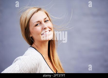 Mädchencharme von nebenan. Porträt einer schönen jungen Frau, die sich draußen vor grauem Hintergrund posiert Stockfoto