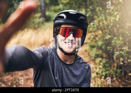 Ein Mann macht ein Selfie, während er auf einem Naturpfad fährt, trägt einen Helm und eine Sonnenbrille. Porträt eines Radfahrers auf einer Fahrradtour durch einen Park oder Wald Stockfoto