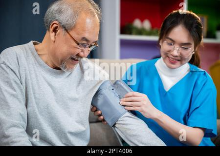 Asiatische Krankenschwester besuchen Patienten Senior Mann zu Hause sie Messung arteriellen Blutdruck auf Arm im Wohnzimmer, Arzt Frau untersuchen tun Überprüfung alten Mann cli Stockfoto