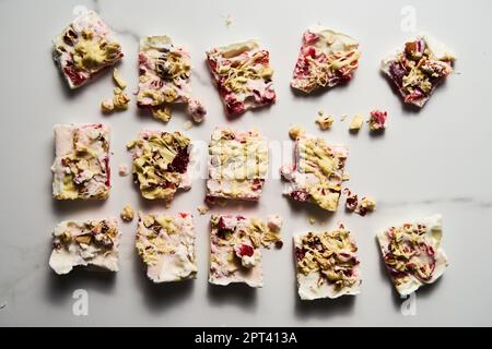 Gesundes gefrorenes griechisches Joghurt mit Erdbeere mit Limettenschale, Nüssen und weißer Schokolade. Hausgemachtes süßes Dessert auf weißem Marmorhintergrund. Draufsicht Stockfoto