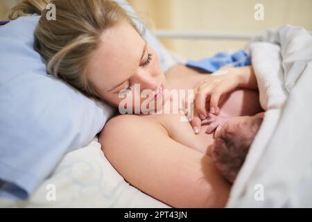 Ihre kleinen Hände werden eines Tages so viele Leben berühren. Eine wunderschöne junge Mutter lag im Bett mit ihrem neugeborenen Mädchen im Krankenhaus Stockfoto