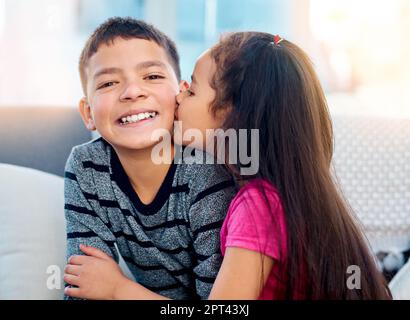 Große Küsse auf die Wange für ihren großen Bruder. Ein bezauberndes kleines Mädchen küsst zu Hause ihren großen Bruder auf die Wange Stockfoto