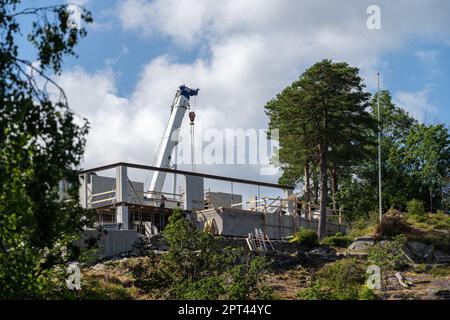 Weißer Mobilkran, der über ein Haus auf einem im Bau befindlichen Hügel ragt Stockfoto