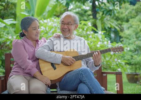 Glückliches asiatisches Seniorenpaar älterer Mann, der Gitarre spielt, während seine Frau zu Hause im Freien zusammen singt, Aktivität, Familiengesundheit, Lebensstil genießen Stockfoto