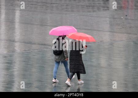 Zwei Frauen mit pinkfarbenem orangefarbenem Regenschirm unter Regen, die vom hinteren Teil aus laufen und kein Gesicht haben. Farbenfroher Regenschirm im Herbst. Selektiver Fokus. Stockfoto