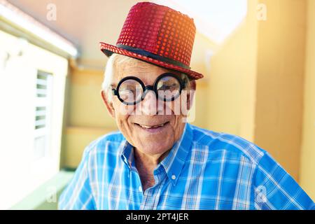 Ich kann durch diese Brille sehen. Ein sorgenloser alter Mann, der eine funky Brille und einen Hut trägt, während er in einem Gebäude für die Kamera posiert Stockfoto