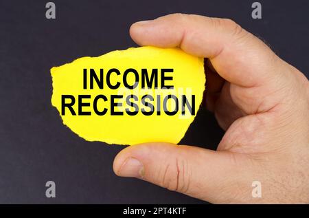 Geschäftskonzept. Auf schwarzem Hintergrund, in den Händen eines Mannes, ein gelber zerrissener Karton mit der Inschrift "Einkommensrezession" Stockfoto