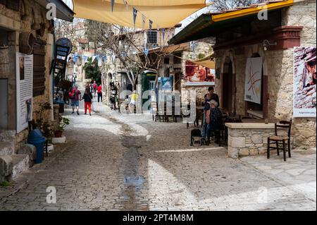 Lofou, Limassol District, Zypern, 24. März 2023 - traditionelle enge Gasse im Dorf mit Geschäften und Restaurantterrassen Stockfoto