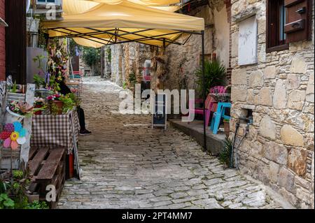 Lofou, Limassol District, Zypern, 24. März 2023 - traditionelle enge Gasse im Dorf mit Geschäften und Restaurantterrassen Stockfoto