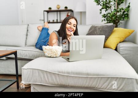 Junge schöne hispanische Frau, die sich zu Hause einen Film ansieht und Popcorn isst Stockfoto