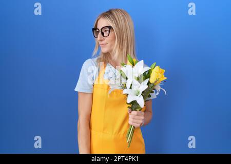 Junge weiße Frau mit Blumenschürze, die Blumen in der Hand hält, mit einem Lächeln auf dem Gesicht, natürlichem Ausdruck. Selbstbewusst lachen. Stockfoto