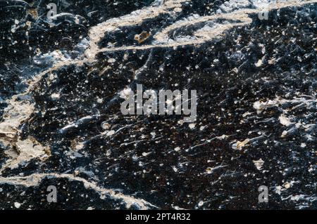 Kontrastreiches Makrofoto von Obsidian mit vielen Blasen, Farben und Verunreinigungen unter der Oberfläche. Stockfoto