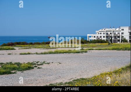 Melanos, Zypern, 25. März 2023 - Kiesstrand, Gras und ein Ferienappartmentblock im Hintergrund Stockfoto