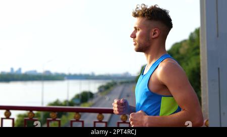 Seitlicher Blick auf einen jungen, gutaussehenden männlichen Athleten, der morgens im Freien trainiert. Schließen. Sportler beim Joggen Stockfoto