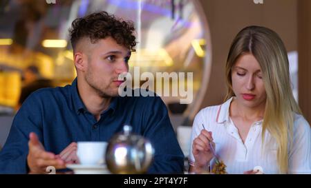 Ein junger, gut aussehender Mann, der mit einer hübschen Frau spricht, während er im Restaurant sitzt. Freund und Freundin zusammen in der Cafeteria in schlechtem Zustand Stockfoto