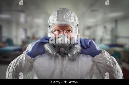 Mann, der einen Gefahrenkanzug, eine Schutzgasmaske und eine Brille trägt, die mit den Händen innerhalb des Krankenhauses bis zum Anschlag reicht. Stockfoto