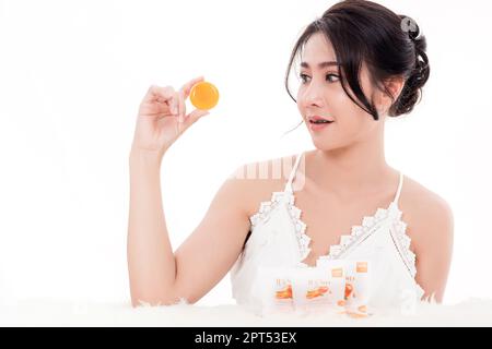 Asiatische junge schöne Frau lächelt sie hält orange handgefertigte Bio-Seife Hautpflege in der Nähe des Gesichts für Present Produkt isoliert auf über weißem Rücken Stockfoto