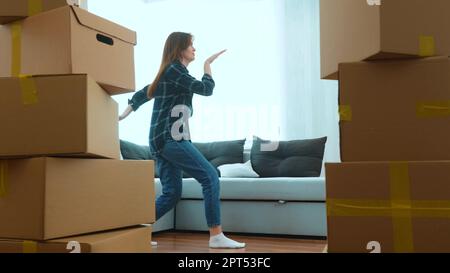 Ein glückliches, positives Paar von Mann und Frau, das im neuen Haus mit vielen Kisten im Zimmer tanzt. Junge Weiße Frau und Ehemann tanzen lustig rein Stockfoto