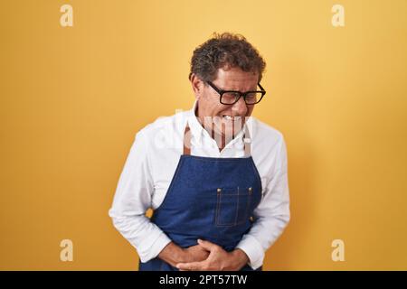 hispanischer Mann mittleren Alters, der eine professionelle Kochschürze mit der Hand auf dem Bauch trägt, weil Übelkeit, schmerzhafte Krankheit Unwohlsein. Ache-Konzept. Stockfoto