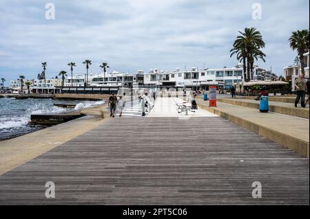 Paphos, Zypern - 27. März 2023 - Holzpier am Strandboulevard mit Palmen und Touristen Stockfoto