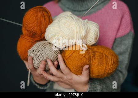 Frauenhände mit farbigen Garnbällen zum Stricken isoliert auf schwarzem Hintergrund. Auswahl an farbenfroher Garnwolle an der Ladenfront. Hausfrauen Stockfoto