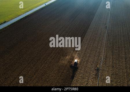 Ein Landwirt, der einen Raupentraktor fährt, zieht eine Staubwolke nach hinten, pflutet die Kruste, die durch die Kraft zerbricht, um Geburt und Aussaat zu erleichtern Stockfoto