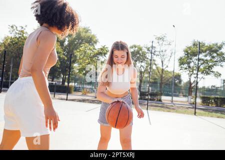 Multikulturelle Gruppe junger Freundinnen, die sich im Freien zusammentun und Spaß haben. Stylische, coole Teenager-Mädchen treffen sich auf dem Basketballplatz, Freunde spielen Stockfoto