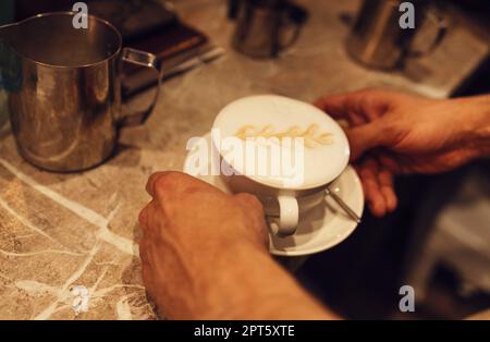 Professioneller Barista, der aufgeschäumte Milch in eine Kaffeetasse gießt, um wunderschöne Latte Art mit Muster herzustellen Stockfoto
