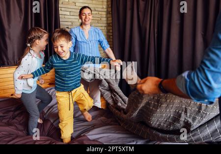 Glückliche Familie, multiethnische Mutter, Vater und Kinder, Sohn und Tochter, lachen, spielen, Bekämpft Kissen und springt ins Bett im Schlafzimmer zu Hause im Stockfoto