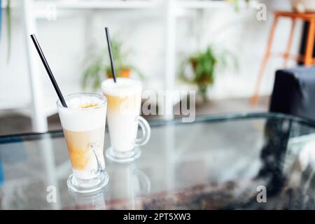 Eiskaffee-Glas auf Holztisch im Restaurant und Café. Zwei Tassen auf dem Tisch Stockfoto