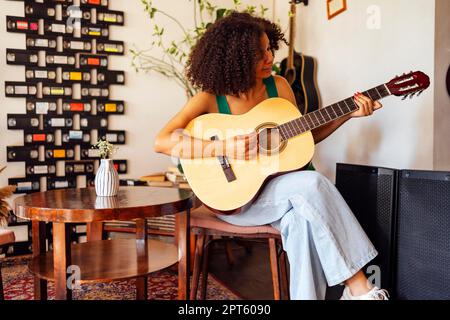 Lächelnde afro amerikanische junge Frau, die akustische Gitarre spielt. Mädchen spielt Gitarre Stockfoto