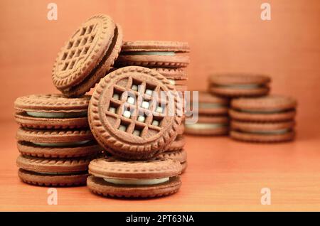 Haufen Chocolate Chip Cookies mit Weiße Vanille Creme gefüllt liegt auf Holz- braune Oberfläche. Süßes und leckeres Sandwich runde Kekse. Detaillierte essen Ph Stockfoto