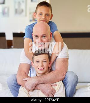Porträt eines jungen kaukasischen Vaters, der zu Hause Zeit mit seinen beiden Söhnen verbringt. Glückliche Geschwister, die sich am Wochenende mit ihrem Vater entspannen. Brüder umarmen Stockfoto