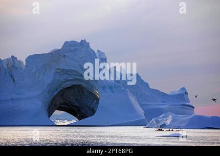 Kajakfahrer vor dem riesigen Eisberg, Eishöhle, Mitternachtssonne, Ilulissat, Disko Bay, Dänemark, Grönland Stockfoto