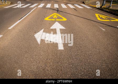 Asphaltstraße mit weißen Pfeilen, Fußgängerüberweg und Wegweisern, die KINDER auf der Straße gemalt haben. Warnung Fahrbahnmarkierung. Stockfoto