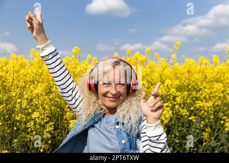 Ältere Frauen hören Musik mit Kopfhörern im blühenden Rapsfeld Stockfoto