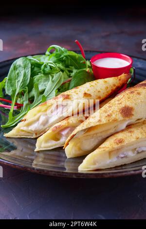 Dünne Pfannkuchen mit Schinken und Käse mit Spinat, Rucola, Mais und Mangold Salat serviert. Stockfoto